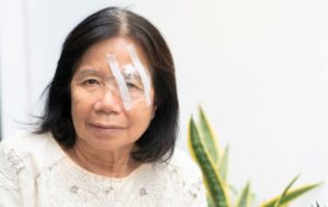 A woman sitting with a shield over her eye, protecting it after cataract surgery