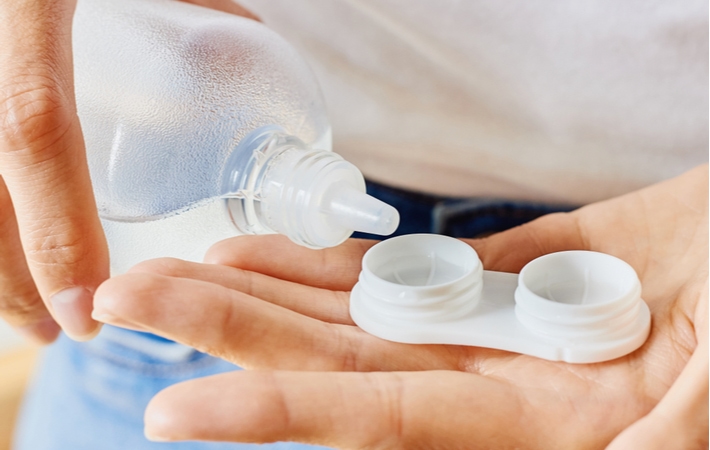 A person holding a contact lens container adding solution with a bottle to the contact lens compartments