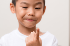 A young boy holding onto a contact lens on his index finger