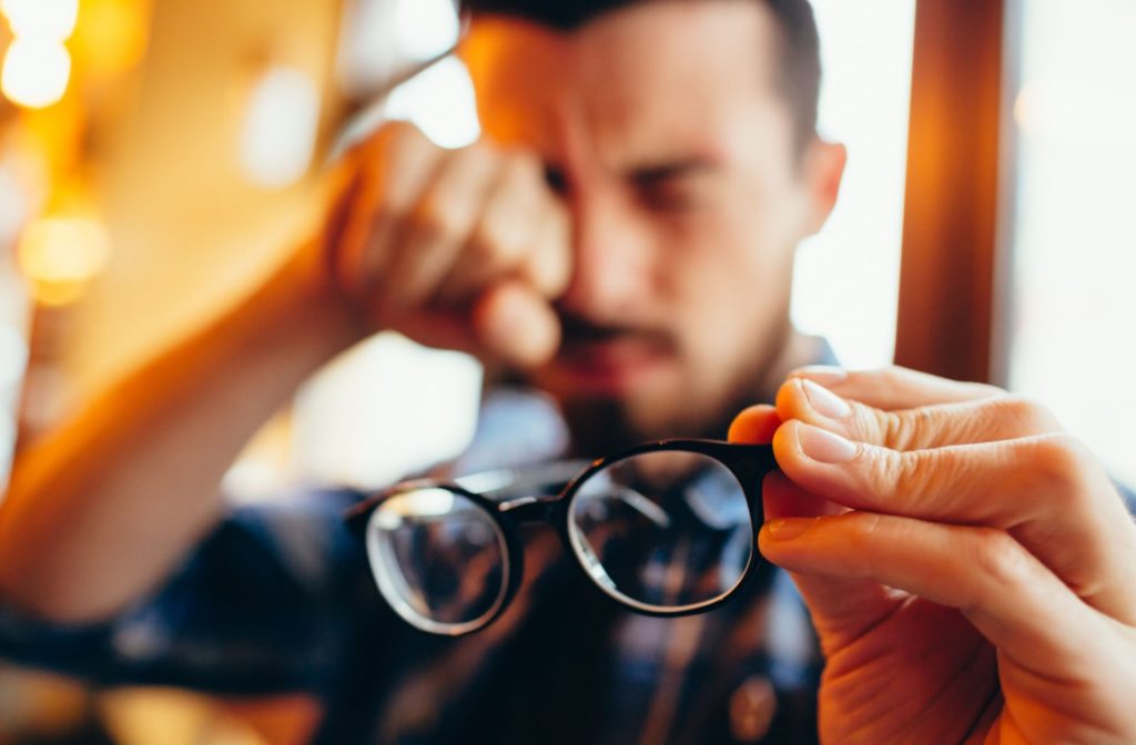 A man removed his eyeglasses and he is rubbing his right eye due to blurry vision
