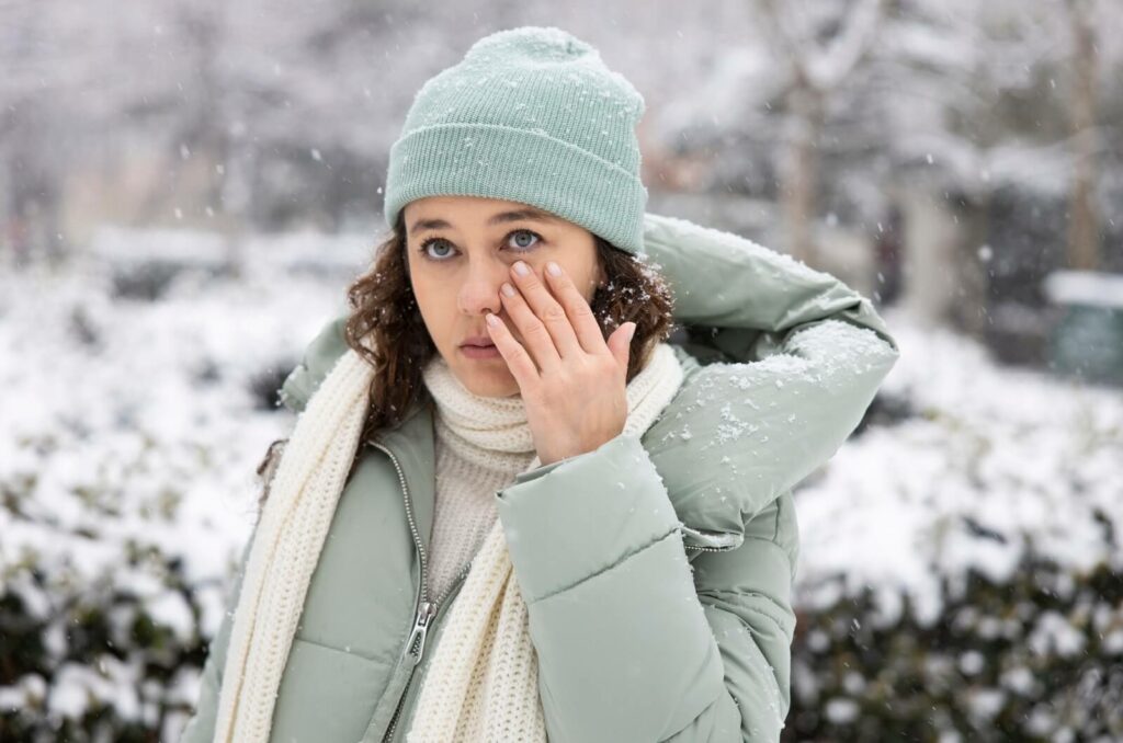 An adult spending time outdoors rubs their irritated eye as they experience dry eyes from the dry winter air.