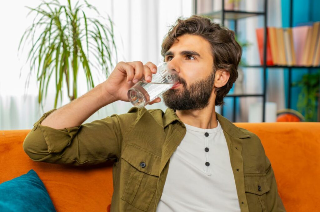 An adult tries to mitigate their chances of getting dry eyes by drinking a glass of water and staying hydrated.