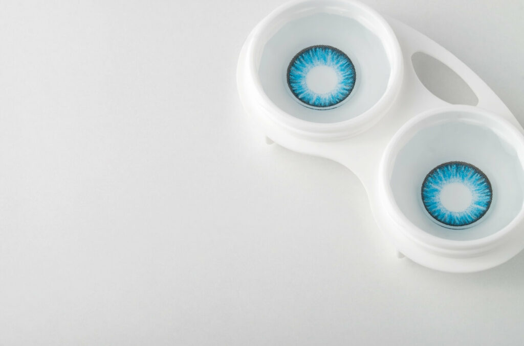 A pair of coloured blue contacts in a contact lens case on a white background.