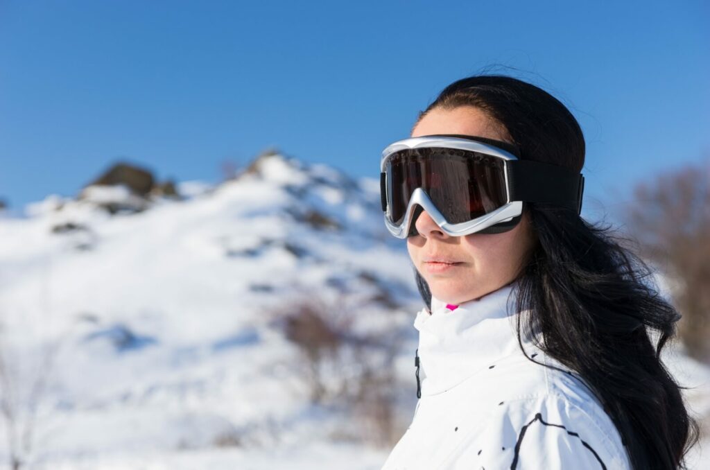 A person standing on a cold mount wears skiing goggles to protect their eyes.