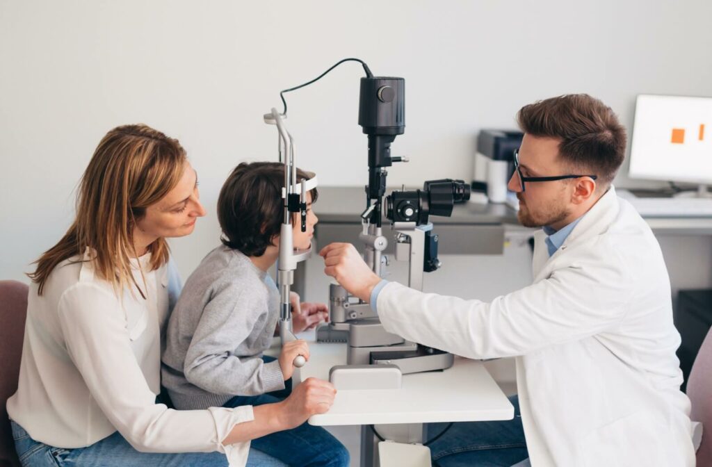 A child sits on their mother's lap while an optometrist uses a retinal camera to examine the child's vision and eyes.