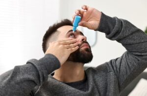 Person putting eye drops into their eyes, with one hand holding their eye open.